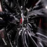 Een werknemer van een cardetailing bedrijf wast het aluminium wiel grondig.