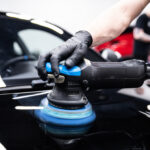 Monteur met zwarte handschoenen die de autolak met een machine polijst in een detailingstudio.